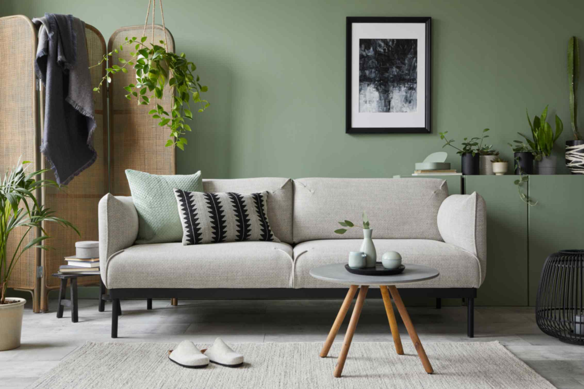 Calming living room interior with sand-colored sofa, wooden elements, and sage green colored wall