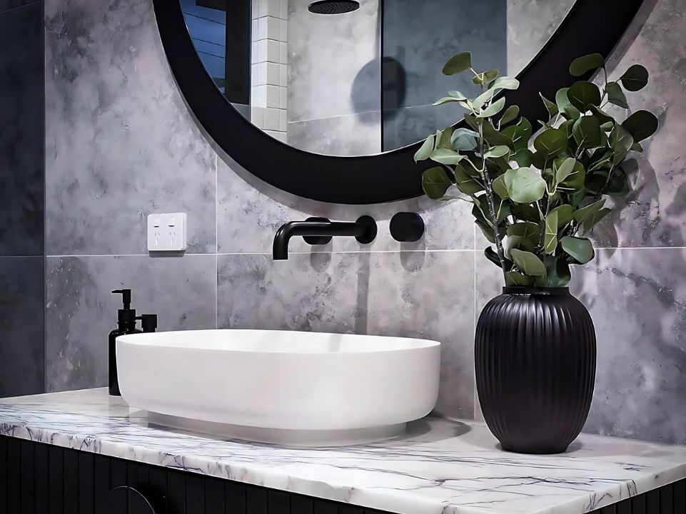 Light gray aesthetic bathroom with white basin black tap and a plant in a black vase