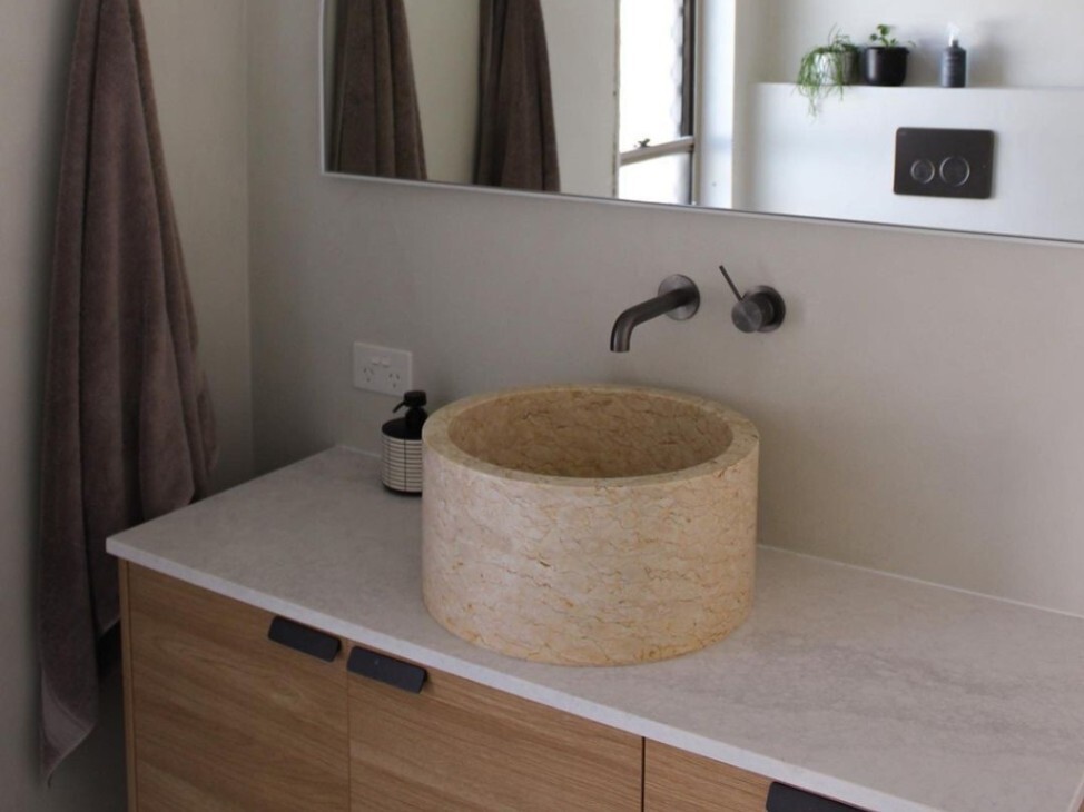 warm marble wash basin with timber cabinetry and Nero Tapware’s black wall-mounted metal tapware